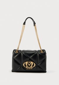 Bolso negro acolchado con herrajes dorados y correa de cadena. Presenta un logo dorado prominente en el frente, textura suave y forma rectangular.