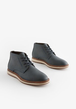 Pánske sivé kožené členkové topánky s modrým prešívaním, guľatou špičkou, šnurovacím dizajnom a béžovou gumenou podrážkou s textúrovaným povrchom.