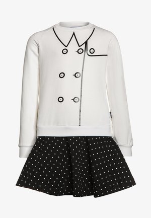 Sudadera blanca con botones y diseño de cuello impresos en negro, combinada con una falda negra con lunares. Tejido de mezcla de algodón, ajuste relajado.