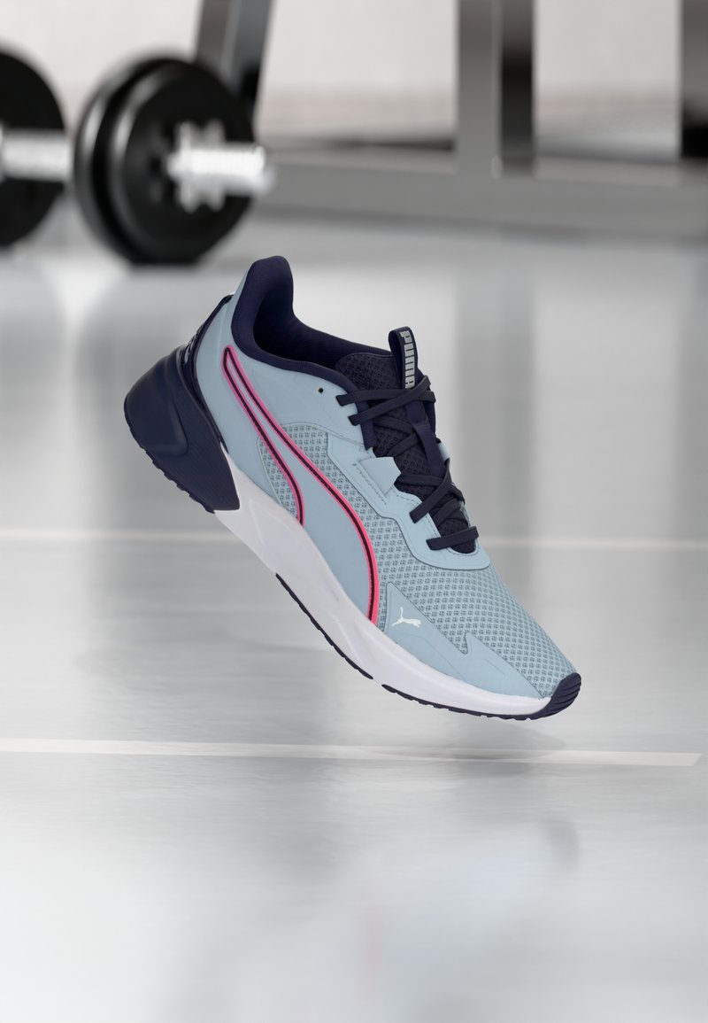 Hellblauer Sportschuh mit dunkelblauen Akzenten, strukturiertem Mesh-Obermaterial, pinken Seitenstreifen und einer gepolsterten weißen Sohle.