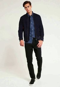 Navy bomber jacket, plaid shirt beneath, black pants, and black slip-on shoes. Smooth fabric, ribbed cuffs, and simple design.