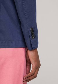 Morska bawełniana koszula z mankietami z czterema czarnymi guzikami i starannie wykończonym dołem, w połączeniu ze jasnoróżowymi spodniami. Widoczna fakturowana tkanina.