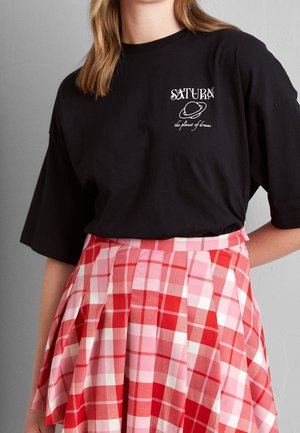 Person wearing a black T-shirt with "Saturn the planet of dreams" text and planet graphic, paired with a red and pink checkered skirt.