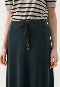 Navyblauwe rok met een koord in de taille en zilveren uiteinden, gemaakt van zachte stof. Gecombineerd met een gestreept lichtbeige en zwarte top.
