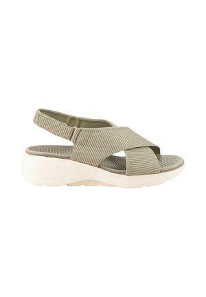 Sandalia beige clara con puntera abierta, gruesas tiras de tela cruzadas, una correa ajustable en el talón y una suela blanca y gruesa con plantilla texturizada.