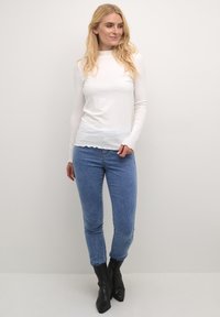 Valge ribadega pikadecottine pluus lainelise äärisega, koos siniste denimipükste ja mustade terava ninaga ankle boots'idega. Lihtne, kehaülene disain.