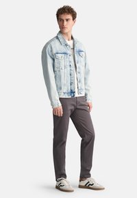 Lichtblauwe denimjack met twee borstzakken, knoopsluiting en vervaagde was, gecombineerd met donkergrijze broek en witte sneakers.