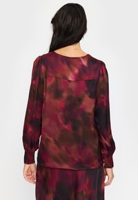 Langermet bluse i multicolert stoff med en gradient av burgunder og brune nyanser. Har en rund hals og smockede mansjetter.