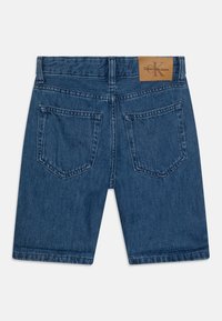 Pantalones cortos de mezclilla en azul oscuro con cinco bolsillos, pasadores para cinturón y una etiqueta de cuero marrón en la parte trasera de la cinturilla. Presenta costuras de doble puntada.