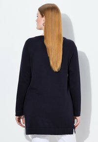 Marinblå långärmad tunika med ribbad struktur, avslappnad passform, sidoslitsar och längd som når under höften, detaljerad med vikta muddar.