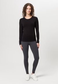 Schwarzes Langarmoberteil kombiniert mit grauen Leggings und weißen Sneakern. Schmale Passform mit glatter Textur, minimalistisches Design und keine sichtbaren Muster.