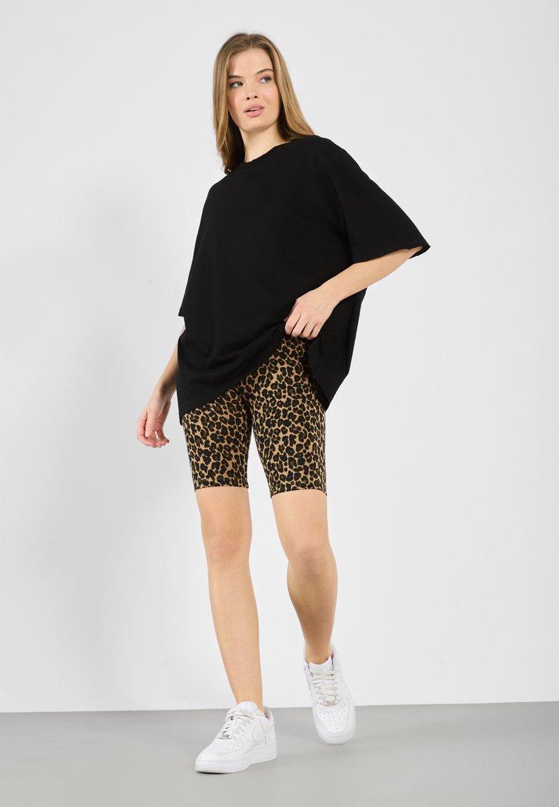 Juodas oversized marškinėliai, leopardų rašto dviratininko šortai ir baltos sportinės bateliai. Švelni medžiaga, laisvas kirpimas, ryškus gyvūnų raštas šortuose.