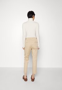 Pantaloni beige a vita alta, vestibilità sartoriale, con tasche posteriori, abbinati a un maglione a collo alto crema aderente e sandali con piattaforma marroni.