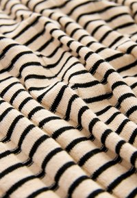 Tissu beige tricoté avec des rayures noires horizontales uniformément espacées, présenté en plis doux avec un détail en gros plan de la texture.