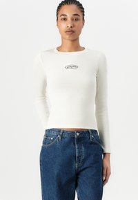 Dlouhý rukáv s jemným ribem v off-white s černou nášivkou "guess jeans". Spárovaný s džíny z modré denimu s vysokým pasem.