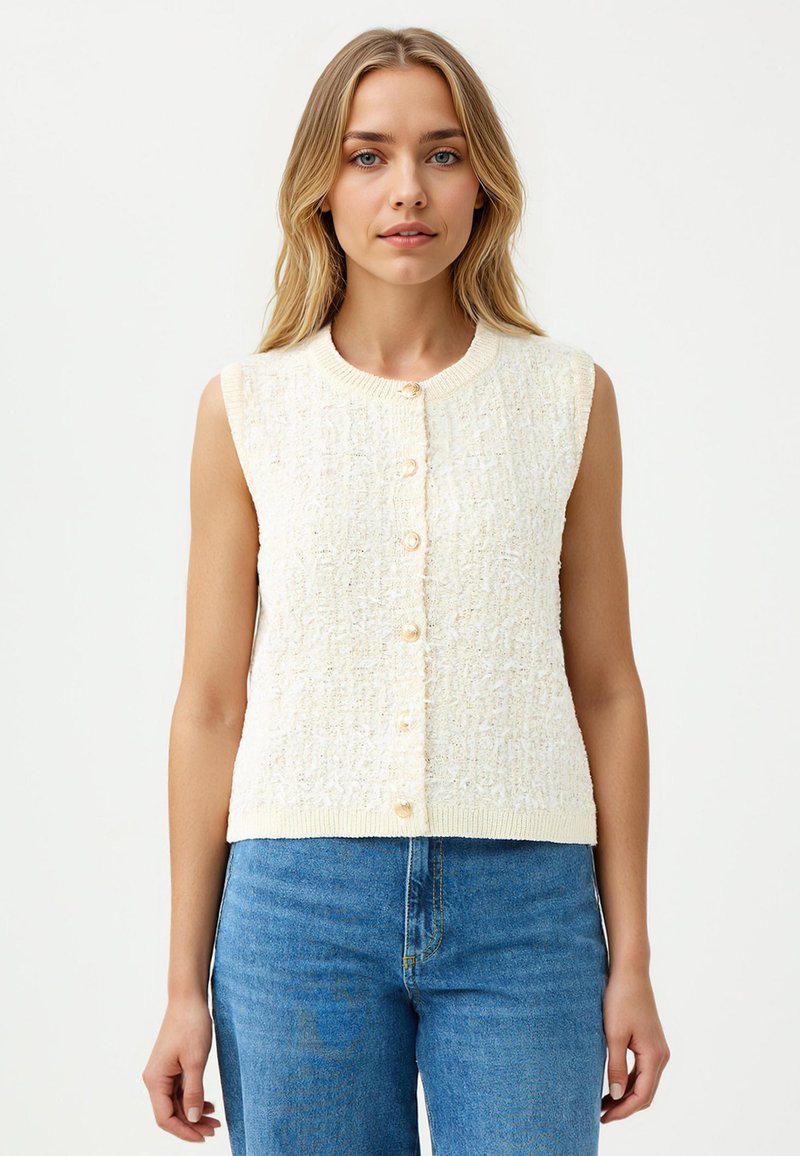 Gilet tricoté sans manches de couleur crème, avec une finition texturée, présentant un col rond et six boutons en perles sur le devant.
