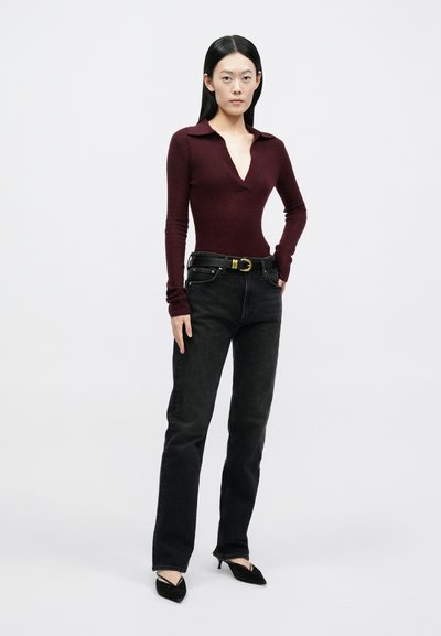 Bordové rebrované body s dlhými rukávmi a hlbokým výstrihom do V, v kombinácii s čiernymi riflemi s vysokým pásom a čiernymi lodičkami s ostrou špičkou.