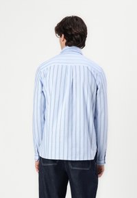 Jasnoniebieska, pasiasta koszula z długimi rękawami, mankietami na guziki i klasycznym kołnierzykiem; wykonana z lekkiego materiału z pionowymi paskami.