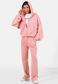 Felpa con zip rosa e pantaloni della tuta abbinati realizzati in tessuto morbido. Presenta un cappuccio, tasche frontali e il marchio "SIXTH JUNE" su entrambi i capi.