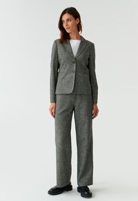 Šedý kostým z vlněné směsi obsahující dobře padnoucí blazer se dvěma knoflíky a volnější kalhoty, doplněný černými platformovými botami.