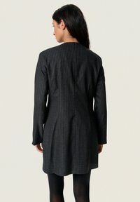 Sötét csíkos ruha áramvonalas siluettal, hosszú ujjakkal, magas nyakkal és ívelt hemvéggel, textúrált anyagból készült.