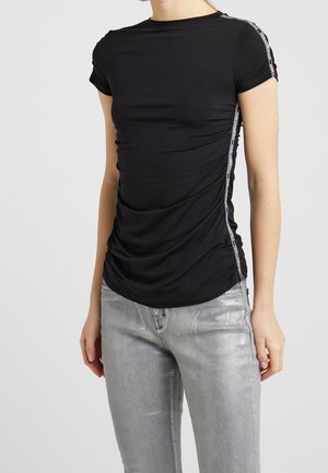 Zwart slim fit top met korte mouwen, gerimpelde zijkanten en wit merkband langs de schouders en zijkanten, gedragen met metallic zilveren broek.