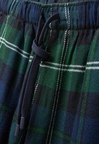 Zelené a modré kostkované pyžamové šortky s elastickým pasem, obsahující šňůrku a bílé akcentní linie v designu. Měkká textilní struktura.