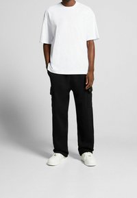 Vit kortärmad t-shirt som matchas med svarta cargo-byxor med sidofickor och vita sneakers med guld-accenter. Avslappnad passform och solida färger.