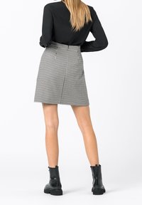 Svart långärmad topp som matchas med en kort, rutigt mönstrad kjol i svart och vitt, med rak skärning och bakfickor. Svarta ankelstövlar.