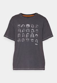Kolkgrå T-shirt med 20 vita minimalistiska ansikts- och frisyrskisser ordnade i ett rutnät, samt en liten "BOSS"-logotyp nere till höger.