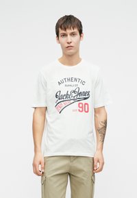 Tricou alb din bumbac cu text imprimat în negru și roșu, având logo-urile "AUTHENTIC SUPPLY CO" și "Jack & Jones". Mâneci scurte, guler rotund.