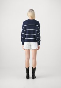 Marinrandig tröja i stickat material med vita horisontella ränder, rund hals, och ribbade ärmslut, kombinerad med vita denimshorts och svarta stövlar.