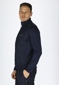 Marine lynlåsjakke med polstret frontpanel, glatte ærmer og to sidelommer. Tekstureret stof på fronten med tætsiddende design.