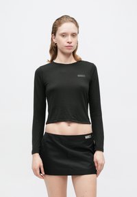 Czarny długi rękaw crop top o dopasowanym kroju z minimalistycznym logo na klatce piersiowej, w połączeniu z czarną mini spódnicą z bocznym metkiem.