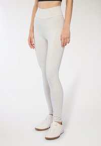 Jasnoszare legginsy o wysokim stanie z gładką fakturą i dopasowanym krojem, zestawione z białymi trampkami z teksturowanym wierzchem i gumową podeszwą.