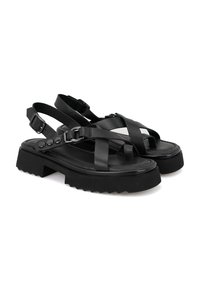 Schwarze Plattformsandalen mit überkreuzten Riemen. Aus Kunstleder gefertigt, mit verstellbaren Knöchelriemen und strukturierten Gummisohlen.