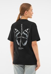 Černé bavlněné tričko s velkým motýlím potiskem v bílé a šedé na zádech, obsahující další text a volný střih.