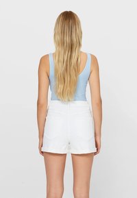 Lichtblauwe geribbelde tanktop gecombineerd met witte denim shorts, met een hoge taille en omgeslagen zoom, gezien vanaf de achterkant.