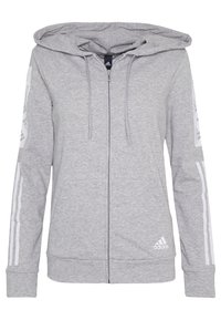 Felpa grigia con zip, dotata di cappuccio, tasche a marsupio, strisce bianche lungo le maniche e logo ricamato sulla parte inferiore sinistra.