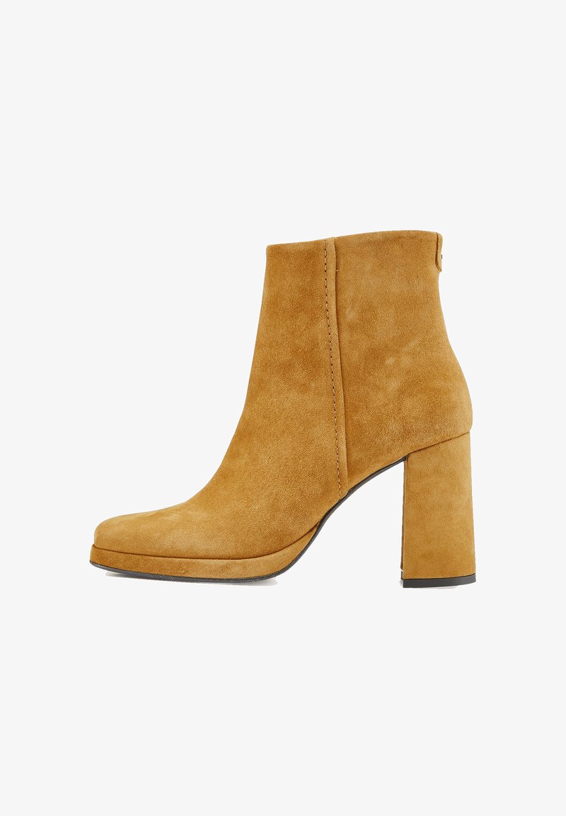 Bottine à talon bloc en daim beige, présentant une texture lisse, un bout arrondi et des détails de couture minimalistes. Design classique et couleur unie.