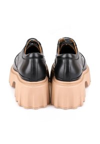 Chaussures en cuir noir à plateforme avec une épaisse semelle beige, présentant un bout arrondi et des détails de couture subtils. Texture lisse et design moderne.