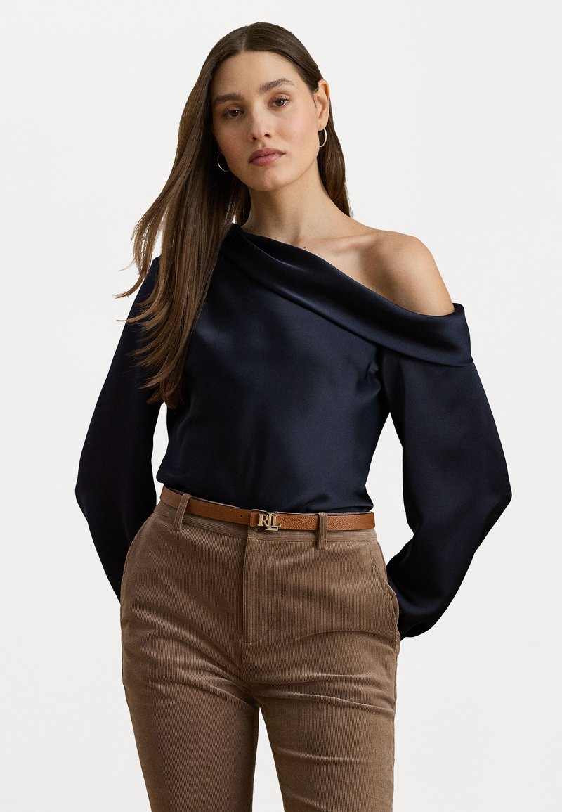Marine satijnen off-shoulder blouse met lange mouwen, gecombineerd met bruine corduroy broeken en een tan riem met een gouden gesp.