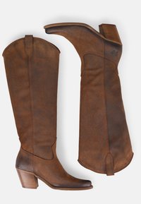 Bottes en suède marron, montantes jusqu'au genou, avec un bout pointu, un talon empilé et des détails de couture. Le matériau présente une texture douce et une finition sourde.