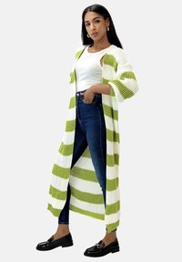 Lång, öppen kofta med gröna och vita ränder, ribbad struktur, trekvartslånga ärmar, kombinerad med figurnära blå jeans och svarta loafers.