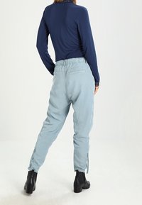 Světle modré kalhoty s uvolněným střihem, elastickým pasem, bočními kapsami a nastavitelnými manžetami, v kombinaci s tmavě modrým topem s dlouhým rukávem a černými botami.