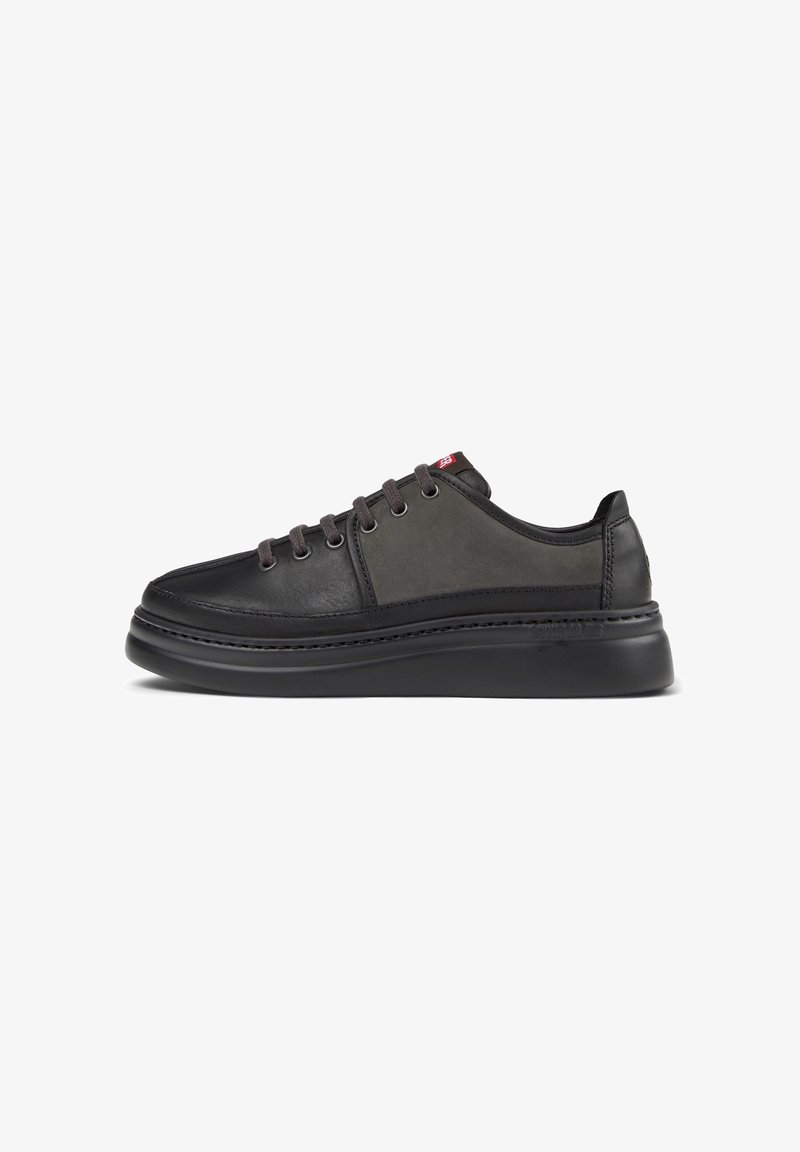 Baskets basses noires et gris foncé avec semelle épaisse, fermeture à lacets et subtil logo rouge de la marque sur la languette, vues de profil.