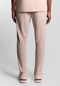 Blanding af bomulds-joggingbukser i blød beige, slim fit med elastisk talje, glat tekstur og tapered ben, parret med lyse sneakers.