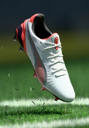 White soccer cleat with a red accent, textured upper, and lace closure. Features a distinctive logo and visible cleats for traction.
