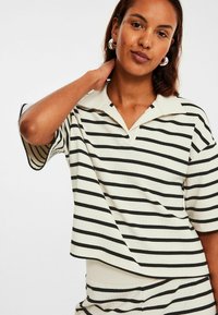 Randiga kortärmade polo med crema och svart, med en enfärgad krage, ribbad textur och avslappnad oversized passform.