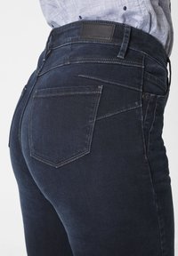 Dunkelblaue Jeans aus Denim mit einer glatten Textur, ausgestattet mit einem Leder-Logo-Patch an der Taille, Gesäßtaschen und kontrastierenden Nähdetails.